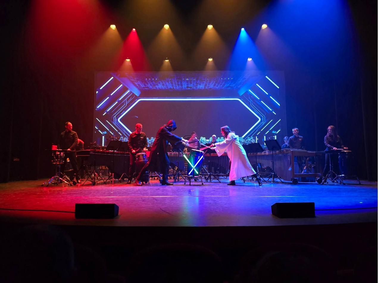 Twee spelers in kostuum doen een zwaardgevecht op een conga, midden op het podium