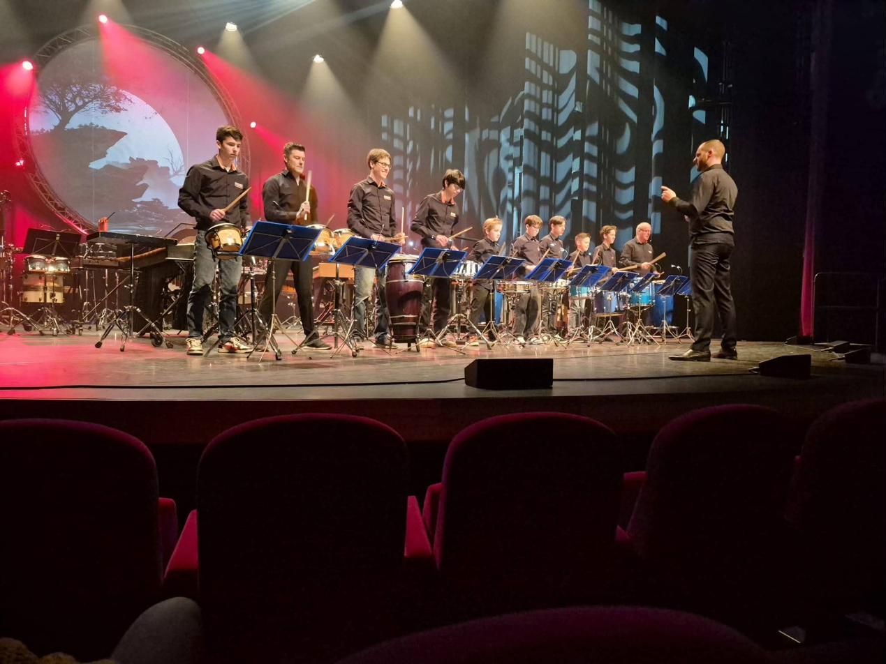 Een rij spelers van jong tot oud op trommels in het theater